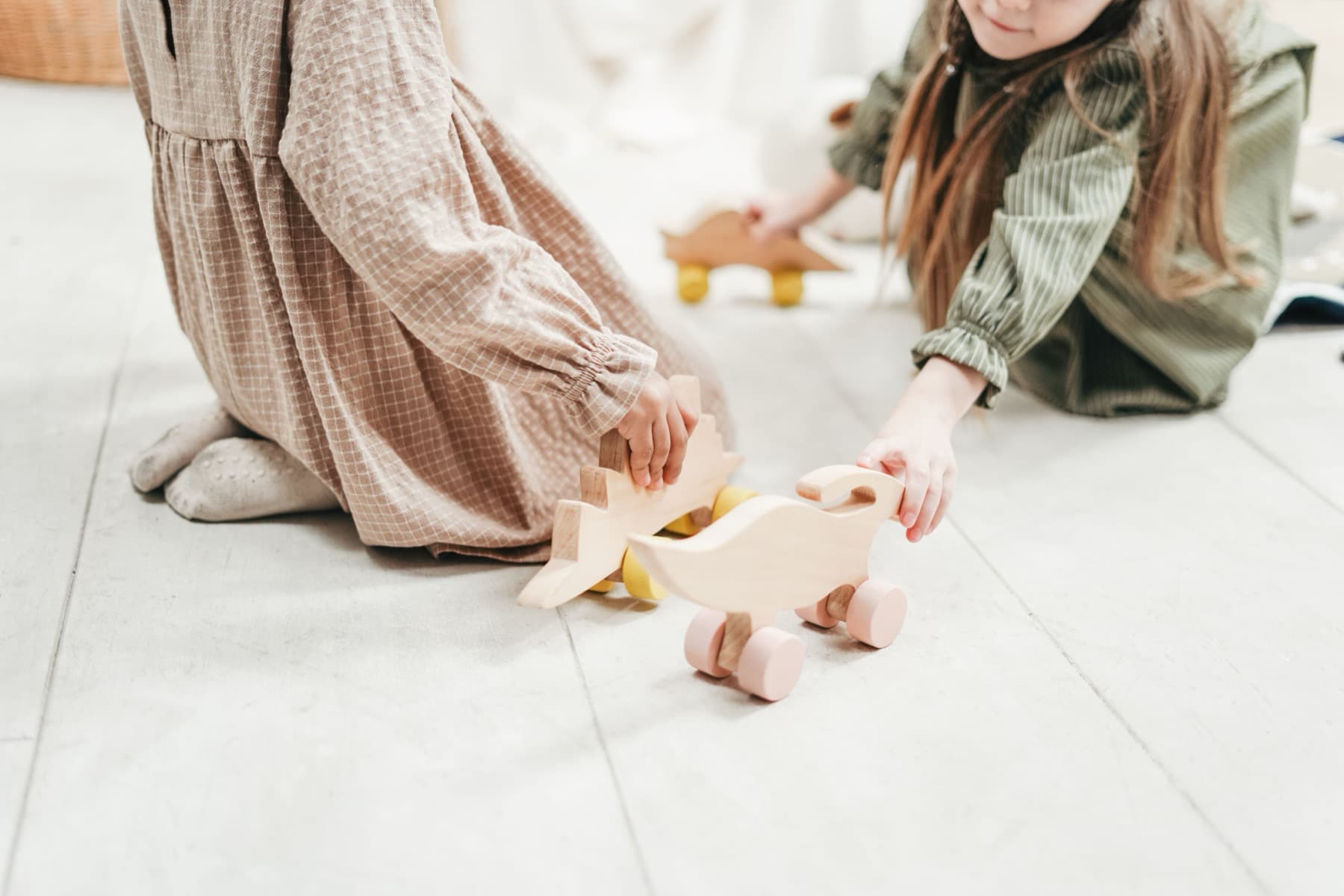 Two children playing with a wooden ride-on duck on a wooden floor